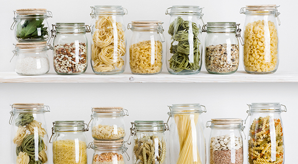 Küchenregal mit Vorratsgläsern, gefüllt mit Nudeln, Linsen, Reis und getrocknetem Gemüse.