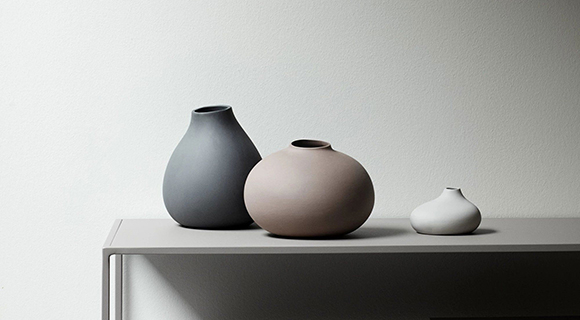 Drei moderne Keramikvasen in Grau-, Beige- und Weißtönen stehen auf einem schlichten Regal. Ihre organischen Formen wirken minimalistisch und betonen das zeitlose Design.