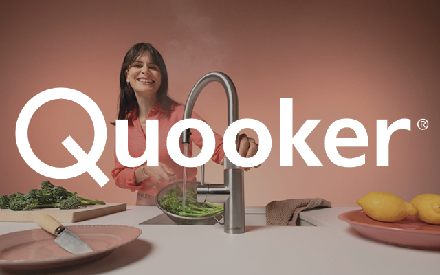 Frau spült Gemüse unter einem modernen Quooker-Wasserhahn in einer hellen Küche, mit großem Quooker-Logo im Vordergrund.