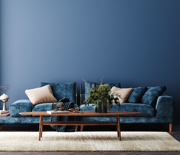 Ein blau gestrichenes Wohnzimmer mit blauem Sofa, dunklen Holztisch, Pflanzen und Dekor.