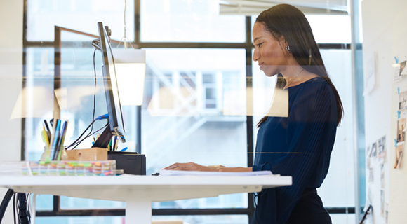 Ergonomischer Arbeitsplatz mit Stehschreibtisch, genutzt von einer Frau in einem hellen Büroraum.