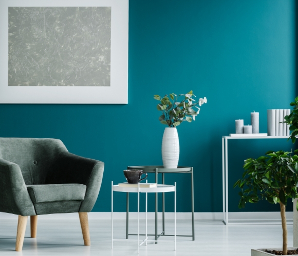 Modernes Wohnzimmer mit blau-grünem Sessel, Stehlampe, Tischen und blauer Wand.