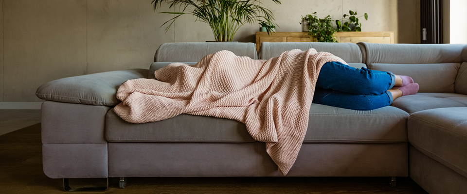 Frau liegt mit Decke über dem Kopf auf einer grauen Schlafcouch