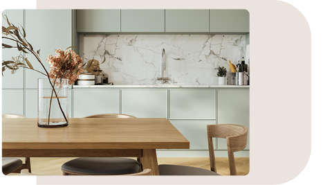 Moderne Küche mit grifflosen, mintgrünen Schränken und einer Rückwand aus weißem Marmor mit grauen Adern. Im Vordergrund steht ein Esstisch aus Holz mit passenden Stühlen. Auf dem Tisch befindet sich eine Glasvase mit trockenen Blumen, die dem Raum eine elegante und natürliche Atmosphäre verleiht