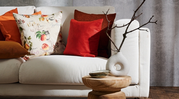 Helles Sofa mit buntem Kissen und einem kleinen runden Beistelltisch aus Holz