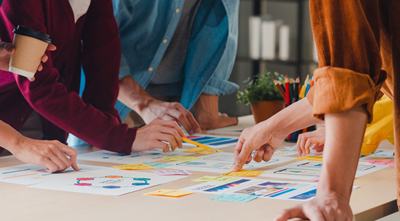 Gruppe von Personen arbeitet gemeinsam an einem Tisch mit Diagrammen, Notizen und Dokumenten.