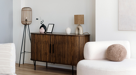 Helles Interieur mit runder Sitzgelegenheit, Holzsideboard und stilvollen Deko-Objekten auf Wandregalen.
