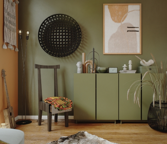 Wohnzimmer mit olivgrüner Kommode, Dekoobjekten, Kunst an der Wand und Holzstuhl auf Holzboden.