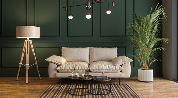 Modern eingerichtetes Wohnzimmer mit beiger Couch, Stehlampe, Deckenleuchte, grüner Wandverkleidung und großer Zimmerpflanze auf Holzboden.