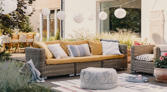 Gem&uuml;tliche Gartenlounge mit mehreren farbigen Sitzkissen steht auf einer modernen Terrasse vorm Haus.