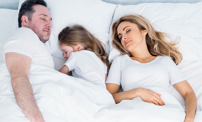 Zwei Erwachsene und ein Kind liegen unter einer weißen Decke