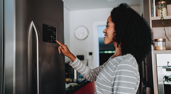 Frau bedient das Display eines modernen Edelstahl-Kühlschranks in der Küche.