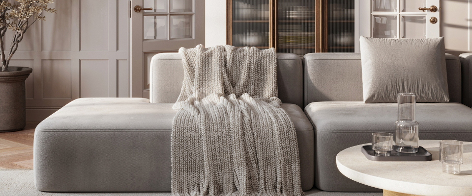 Modernes Wohnzimmer mit grauem Sofa, beigefarbener Strickdecke und rundem Couchtisch