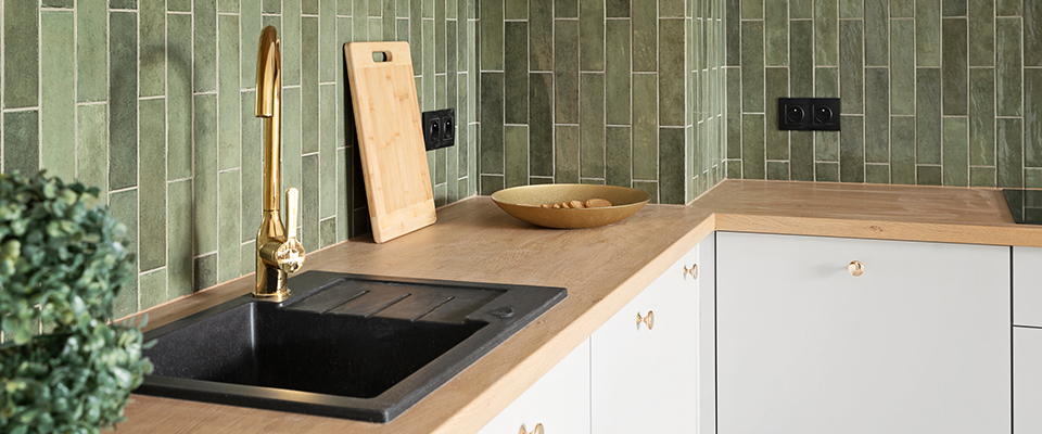 Moderne Küchenzeile mit grüner Fliesenrückwand, schwarzer Spüle und goldener Armatur.