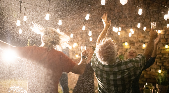 Ausgelassene Feier im Freien bei Nacht mit funkelnden Lichterketten und sprühendem Regen.