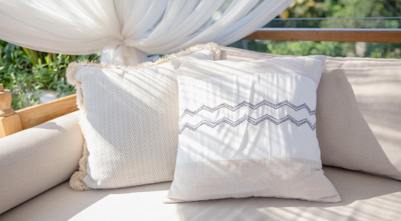 Zwei beigefarbene Kissen mit Struktur und Ziern&auml;hten auf einer gepolsterten Gartenbank.