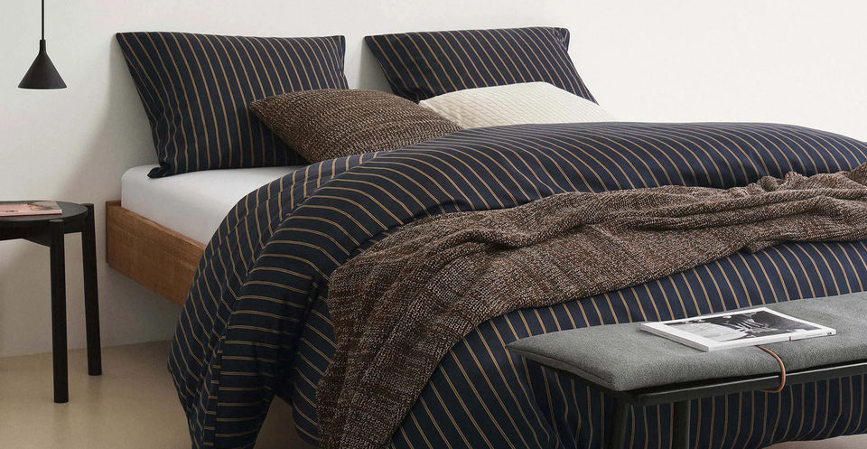 Das Schlafzimmer wurde schlicht eingerichtet. Auf dem Bett liegen Decken und Kissen mit schwarzen Bezügen.
