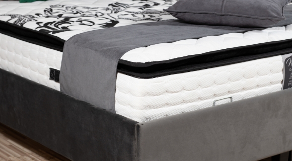 Detailansicht eines Boxspringbetts mit sichtbarem Matratzenaufbau und Topper, bezogen mit grauem Stoffbezug
