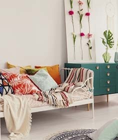 Boho-Wohnzimmer mit bunter Couch, Kissen, Decke und Blumenwanddeko