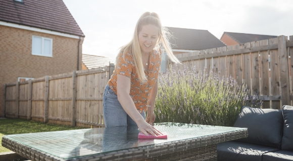Eine Frau putzt die Tischplatte des Gartentisches mit einem Tuch ab.
