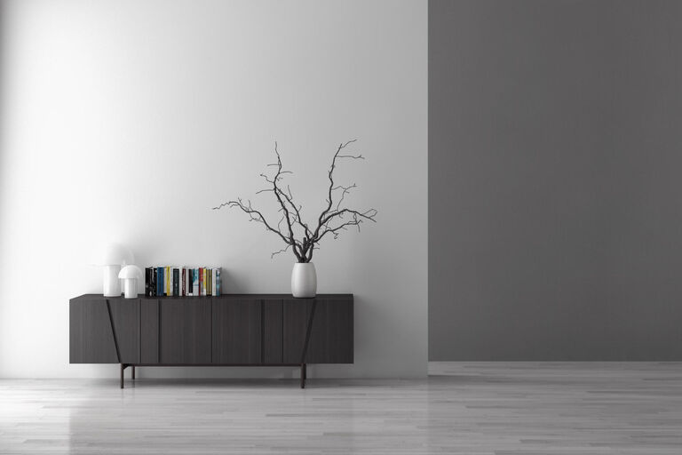 Ein schwarzes Lowboard steht mit Büchern und dekorativen Ästen in einer Vase vor einer weißen Wand