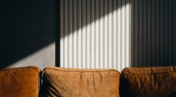 Lichtdurchflutete Szene mit braunem Ledersofa vor geriffelter Wandverkleidung