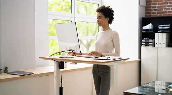 Frau arbeitet an einem Computer im Stehen an einem höhenverstellbaren Schreibtisch in einem modernen Büro.