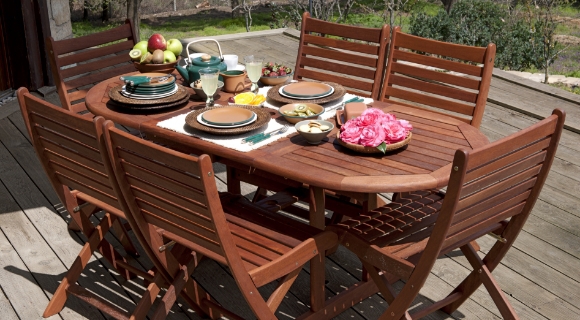 Holzterrasse mit ovalem Gartentisch, sechs Klappst&uuml;hlen und gedecktem Geschirr im Au&szlig;enbereich.
