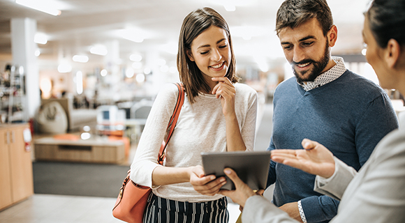 Verkäuferin berät ein junges Paar mithilfe eines Tablets in einem modernen Geschäft.
