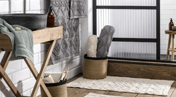 Bad im Ethno-Stil mit Holzdetails, Badteppichen und gewebten Körben vor schwarzer Glasdusche.