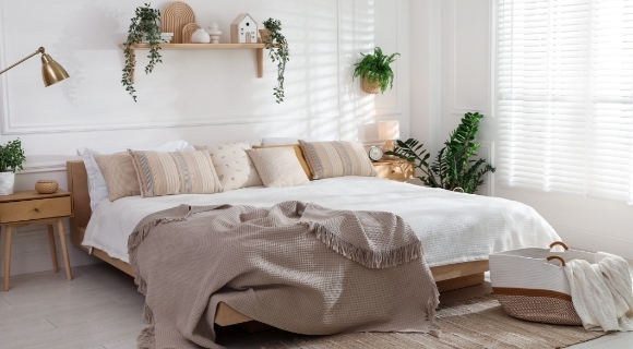 Holz Bett, auf dem mehrere Kissen liegen sowie eine braune Tagesdecke. 