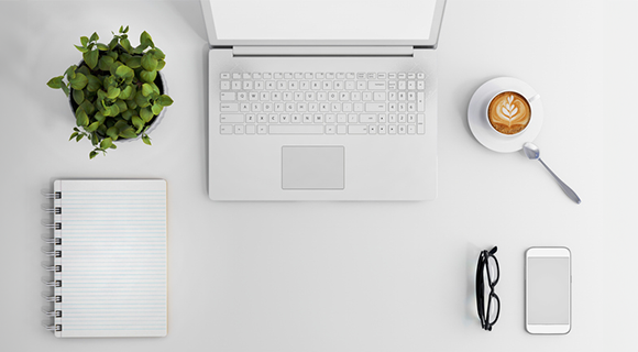 Aufgeräumter Arbeitsplatz von oben mit Laptop, Notizbuch, Smartphone, Brille, Kaffee und Pflanze.