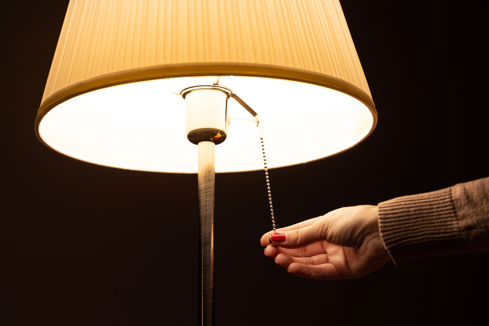 Nahaufnahme einer Hand, die eine Stehlampe mit Zugkette einschaltet.