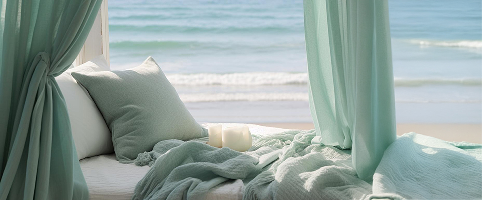 Himmelbett mit mintgrüner Bettwäsche und Kissen vor offener Meersicht, lichtdurchflutet und sommerlich – entspannte Atmosphäre am Strand
