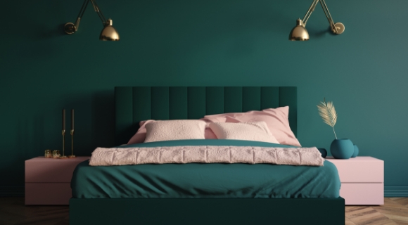Farbintensives Schlafzimmer mit Boxspringbett in Petrolgrün, pastellrosa Akzenten und goldenen Wandlampen – harmonisches Farbkonzept mit starker Raumwirkung