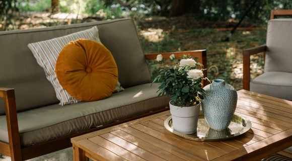 Ein Garten Sofa und ein Tisch aus Holz mit erdfarbigen Kissen und Blument&ouml;pfen.