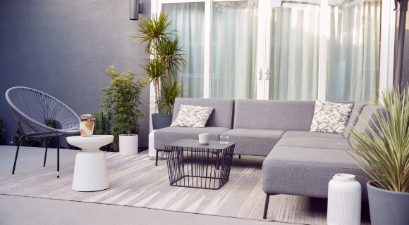 Schwarzes Outdoor Sofa mit grauen Polstern und wei&szlig;-grauen Kissen als Akzent. 