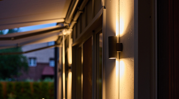 Moderne Außenwandleuchte an Hausfassade mit warmem Lichtschein in den Abendstunden.