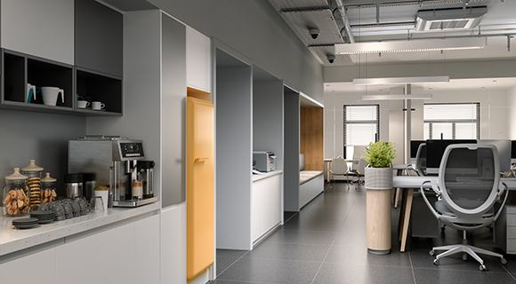 Moderne, helle Büroküche in einem offenen Großraumbüro. Links im Bild befindet sich eine Küchenzeile mit weißen Unterschränken, dunklen offenen Regalen und einer großen silbernen Kaffeemaschine mit Tassen und Gläsern daneben. Auf der Arbeitsfläche stehen außerdem ein Glasbehälter mit Gebäck und ein Heißwasserspender. Ein auffälliger gelber Kühlschrank setzt einen farblichen Akzent. Dahinter erstreckt sich ein langer Flur mit verschiedenen Nischen und Geräten, wie einem Drucker. Rechts ist der offene Bürobereich mit ergonomischen Bürostühlen, Schreibtischen, einem runden Pflanzgefäß und großen Fenstern zu sehen. Die Gestaltung ist hell, funktional und freundlich – ideal für Pausen und produktives Arbeiten.