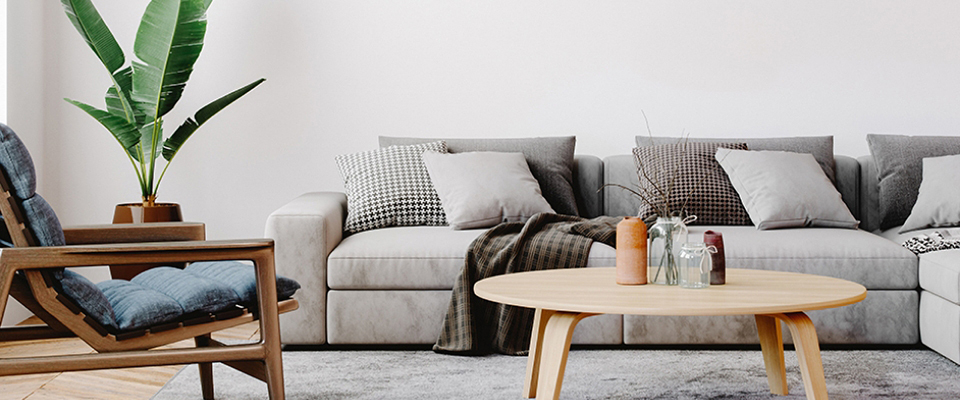 Helles Wohnzimmer mit grauer Couch, Sessel und rundem Couchtisch