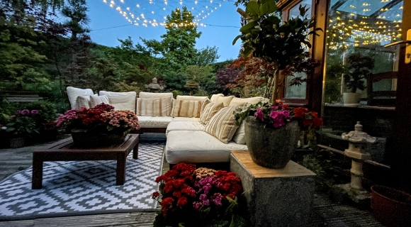 Gem&uuml;tliche Gartenterrasse mit wei&szlig;er Lounge-Ecke, Lichterkette &uuml;ber dem Sitzbereich und bepflanztem Au&szlig;enbereich.