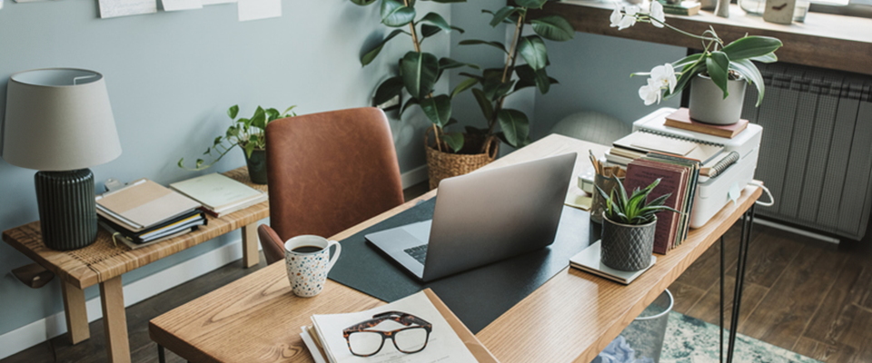 Homeoffice-Schreibtisch aus Holz mit Laptop, Büchern und Pflanzen.