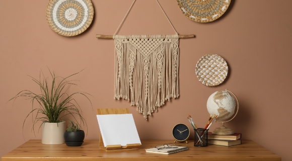 Boho-Arbeitsplatz mit Makramee-Wanddeko, Holztisch, Pflanzen, Globus, Uhr und natürlichen Accessoires