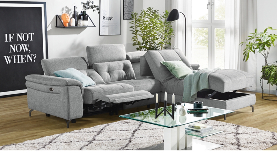 helles Wohnzimmer mit vielen Bildern an der Wand, einer grauen Couch und einem Couchtisch mit Glasplatte