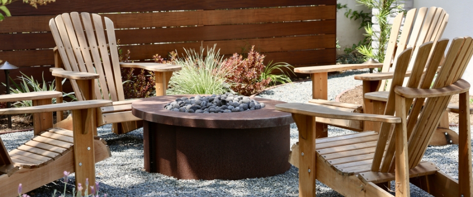 Gartensessel stehen vor einer Feuerschale im Garten.