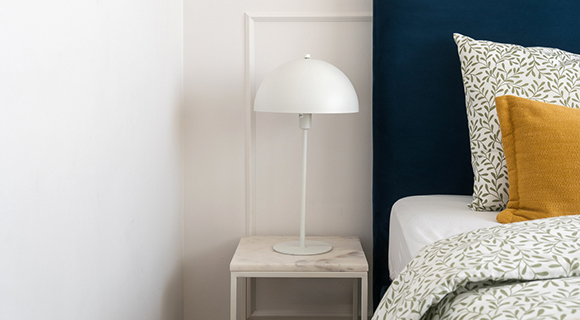 Modernes Schlafzimmer mit blauem Kopfteil, weißem Nachttisch und minimalistischer Tischlampe im skandinavischen Stil.