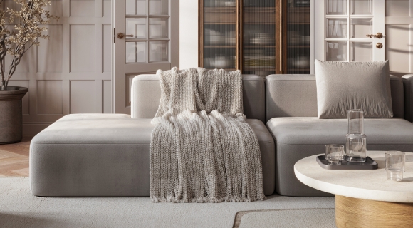 Modernes Wohnzimmer mit grauem Sofa, beigefarbener Strickdecke und rundem Couchtisch