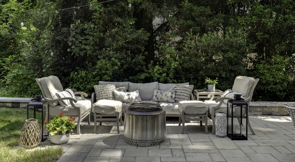 Terrassen-Sitzgruppe im Garten mit Outdoor-Sofa, Sesseln, Beistelltischen und zentraler Feuerstelle.