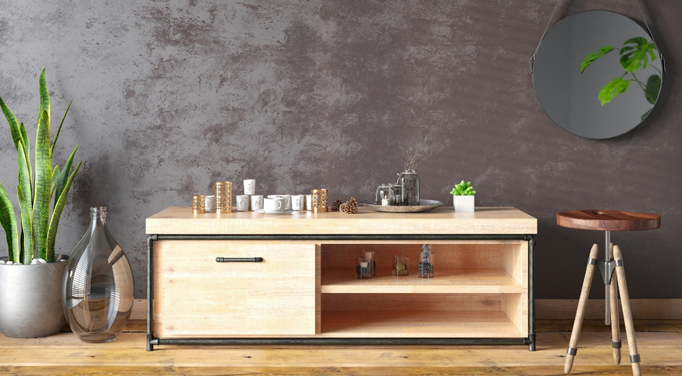 niedrige Kommode in hellem braun, daneben ein Hocker, eine Pflanze und ein Spiegel an der Wand