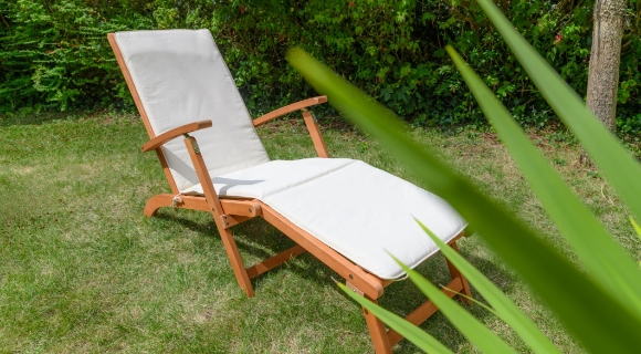 Holz-Gartenliege mit wei&szlig;er Polsterauflage steht auf einer Rasenfl&auml;che.